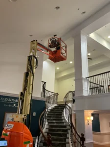 Electrician on a lift inspecting a recessed light fixture to troubleshoot flickering LED bulbs in a Savannah Retirement Community
